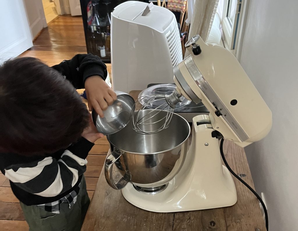 Child putting ingredients into the macaron mixing machine, hands in action